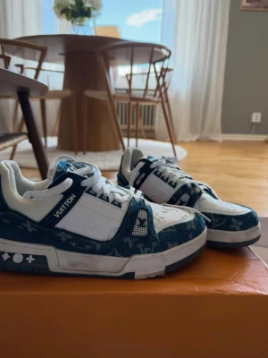 Louis Vuitton blåvita sneakers - Säljer ett par Louis Vuitton sneakers i blått och vitt med klassiskt monogrammönster. Skorna har vita detaljer, blå denimliknande partier och tydliga LV-loggor på sidan. Snygg och modern design med robust sula och lågt skaft.