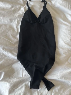 Svart body med smala axelband - Snygg svart body med smala justerbara axelband och v-ringad urringning. Bodyn har en enkel, stilren design och är tillverkad i ett stretchigt material som formar sig efter kroppen. Passar att använda under t.ex en kofta eller bara som den är❣️
