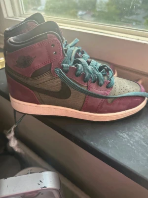 Vinröda och svarta high-top sneakers - Snygga high-top sneakers i vinrött och svart med gröna skosnören. Skon har en klassisk siluett med svart swoosh på sidan och detaljer i mocka och textil. Perfekt för dig som vill sticka ut med färg och stil. storlek 36