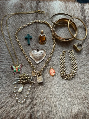 Mix av vintage smycken i guldton - Samling med flera smycken i guldton, inklusive armband, halsband, berlocker, brosch och ring. Materialen är olika metaller prydda med emalj och pärlor. Perfekt för dig som gillar unika accessoarer och retrostil. Budas ut på min live 25 augusti 19.00! 