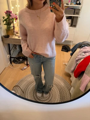 Ljusrosa stickad tröja - Mysig ljusrosa stickad tröja med rund halsringning och långa ärmar. Tröjan har en avslappnad passform och ribbstickade muddar vid ärmslut och nederkant. Perfekt för att hålla värmen under kyliga dagar.