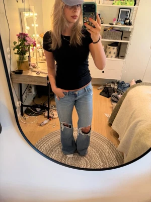 Ljusblå slitna bootcut jeans - Säljer ett par ljusblå bootcut jeans med stora slitningar över knäna och råa kanter. Jeansen har en avslappnad passform och klassisk femficksdesign. Perfekta för en trendig och avslappnad look.