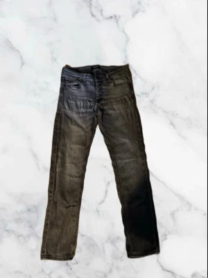 Jack and Jones Jeans  - Säljer ett par mörkgrå jeans med rak passform och klassisk femficksdesign. Jeansen har en snygg tvättad look och är tillverkade i ett slitstarkt denimtyg. Perfekta för dig som gillar en enkel men cool stil. W30 L30