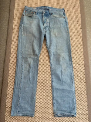 Levis 501 W30 L32 - Säljer ett par klassiska ljusblå jeans med rak passform och fem fickor. Jeansen har normal midja och är tillverkade i denim med synliga sömmar. Perfekta för en avslappnad och tidlös stil. Bra skick 