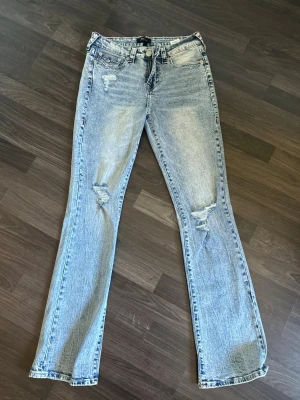 True Religon bootcut  - Säljer ett par ljusblå True Religon Becca midrise bootcut jeans med slitna detaljer på låren och knäna. Röda snygga stygn med den klassiska bakfickan. Materialet är klassisk denim i bomull. Säljer pga dom är för stora för mig och därmed inte används alls. Skicket är fint inga tecken på slitage eller fläckar. 