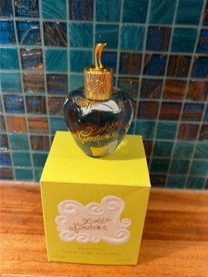 Lolita Lempicka Eau de Parfum 30ml - Lolita Lempicka Eau de Parfum i en unik, hjärtformad flaska med blå och guldiga detaljer. Flaskan rymmer 30 ml och kommer i en gul förpackning med vita och guldiga inslag. Doften är elegant och flaskan är en riktig eye-catcher på parfymhyllan. Nytt skick!