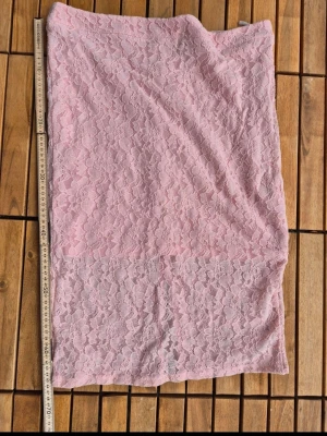 Ljusrosa spetskjol med slits - Säljer en ljusrosa långkjol i spets med blommigt mönster. Kjolen har en snygg slits bak och är fodrad undertill för extra komfort. Perfekt för dig som vill ha en feminin och trendig look.