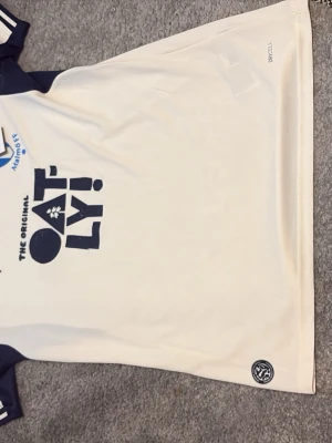 Malmö FF matchtröja Puma beige - Snygg beige matchtröja från Malmö FF med mörkblå detaljer och Oatly-logga på bröstet. Tröjan har klubbmärke, Puma-logga och rund hals med blå kant. Tillverkad i funktionsmaterial för sport och träning.