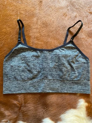 Grå sport-bh med svarta band - Säljer en gråmelerad sport-bh med tunna, justerbara svarta axelband. Bh:n har en enkel och bekväm design utan byglar och är tillverkad i ett mjukt, stretchigt material som passar perfekt till träning eller vardag.