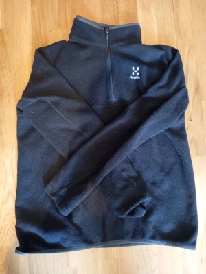 Svart fleece tröja från Haglöfs - Mysig svart fleece tröja från Haglöfs med halv dragkedja och hög krage. Perfekt för kyliga dagar och outdoor-äventyr. Tröjan har lång ärm och diskret logga på bröstet. Tillverkad i mjukt fleecematerial. Den är knappt använd. Pris kan diskuteras🙌. Mvh Rasmus