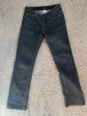 Mörkblåa lågmidjade straight jeans - Snygga mörkblå lågmidjade jeans med straight passform och är i storlek W28 L32. Jeansen har kontrastsömmar och silverfärgade nitar. Tillverkade i ett mjukt denimtyg som sitter bekvämt. Perfekta till en avslappnad stil.