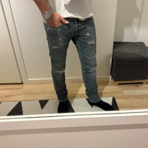 Replay jeans  - Säljer ett par blå jeans med slitningar och lätt tvättad look. Jeansen har klassisk femficksmodell och smal passform som sitter tajt längs benen. Perfekta för en avslappnad och trendig stil.