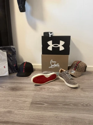 Christian Louboutin  - Snygga gråa sneakers från Christian Louboutin med klassisk röd sula och vita kanter. Box osv tillkommer. Skorna har lågt skaft, snörning och är tillverkade i mocka för en lyxig känsla. Perfekta för dig som vill sticka ut med exklusiva detaljer.