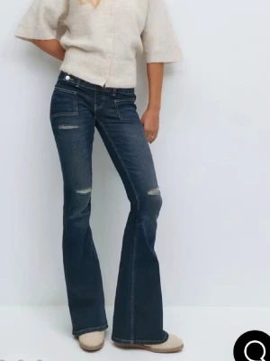 Blå bootcut jeans med slitningar - Snygga blå bootcut jeans med slitningar på benen och två knappar i midjan. Jeansen har framfickor och bakfickor, samt en lätt tvättad look. Perfekta för dig som gillar en avslappnad och trendig stil. Helt som nya!!