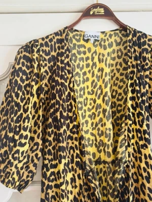 Leopardmönstrad långklänning från Ganni - Säljer en maxad långklänning från Ganni med leopardmönster i gult och svart. Klänningen har puffiga korta ärmar och en djup v-ringning. Perfekt statement piece för dig som vill sticka ut. Materialet känns lätt och flowy. Omlott klänning passa storlek 34-36 perfekt.