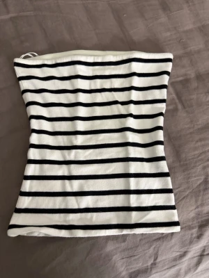 Randig tubtopp från BikBok XS - Säljer en vit tubtopp med svarta horisontella ränder från BikBok i storlek XS. Toppen är axelbandslös och har en enkel, tight passform som sitter snyggt på kroppen. Perfekt för sommardagar eller att styla lager på lager.