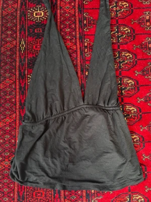 Svart halterneck topp med knyt brandy melvilöe - Säljer en svart halterneck topp med djup urringning och knyt i ryggen. Toppen är ärmlös och har en croppad passform, perfekt för att styla med höga jeans eller kjol. Tillverkad i mjukt bomullstyg för en bekväm känsla.