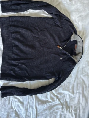Mörkblå halvzip tröja från Morris - Snygg mörkblå tröja från Morris med halvzip och liten broderad logga på bröstet. Tillverkad i 100% merinoull och har kontrastfärgad insida på kragen. Perfekt för lager på lager och stilrena outfits. Sitter fint överlag passar dig om du är runt 170 eller under. Nypris 1399 mitt pris är 360