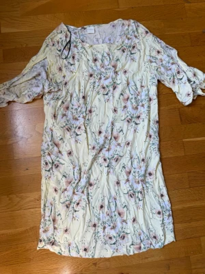 Blommig ljus kortklänning med volang - Söt kortklänning i ljusgul ton med blommigt mönster i rosa och grönt. Klänningen har volangdetaljer och korta ärmar med knyt. Perfekt för sommarens alla tillfällen! . Skriv privat för fler bilder eller om du har några frågor💗