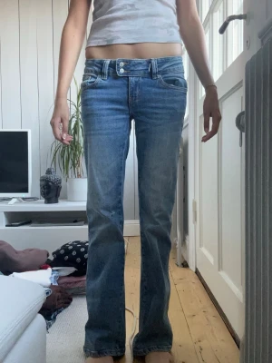Blå bootcut jeans med låg midja - Snygga blå bootcut jeans med låg midja och klassiska fickor. Jeansen har en lätt tvättad look och raka ben som går ut lite nertill. Perfekta för en avslappnad och trendig stil.