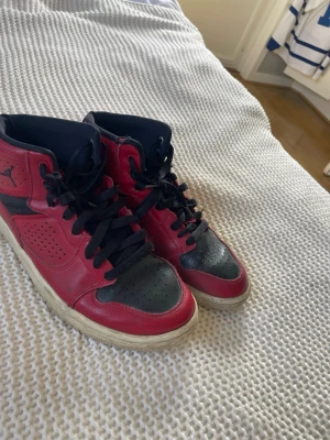 Röda och svarta Jumpman/Jordan sneakers - Snygga sneakers i rött och svart med klassisk Jumpman/Jordan-logga på sidan och texten 'JUMPMAN.' på plösen. Skorna har svarta skosnören, perforerade detaljer och vit sula. Tillverkade i läder och textil för en sportig look.