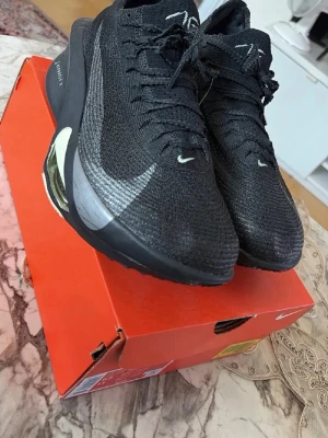Nike Vaporfly 3 svarta sneakers - Nike Vaporfly 3 sneakers i svart med stickad ovandel och reflekterande detaljer. Skorna har en synlig Zoom Air-enhet i sulan och en stor silverfärgad Swoosh på sidan. Lätta och sportiga med modern design och snörning.