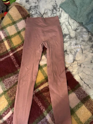 Stronger tränings byxor  - Stronger träningsbyxor, Säljer ett par snygga rosa leggings med ribbad struktur och hög midja. De har diskreta ränder längs benen och är stretchiga för en bekväm passform. Perfekta för en trendig och avslappnad stil.