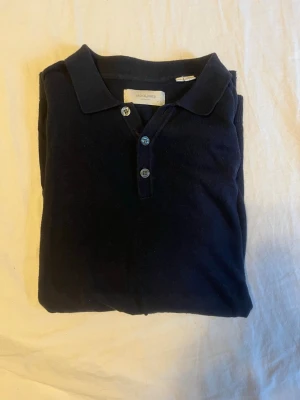Stickad piké , Jack & Jones - Snygg mörkblå piké från Jack & Jones med klassisk krage och tre knappar framtill. Tillverkad i mjukt material och har en enkel, stilren look som funkar till det mesta.
