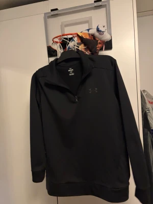 Svart half-zip tröja Under Armour - Svart half-zip tröja från Under Armour i loose fit. Tröjan har hög krage, långa ärmar och diskret logga på bröstet. Använd 3 gånger 