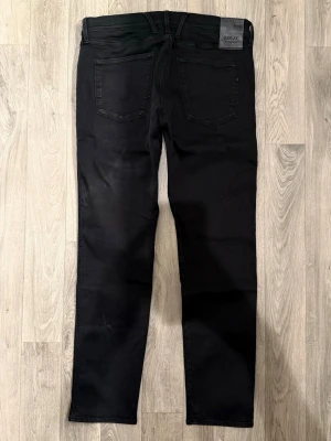 Replay Anbass Hyperflex Jeans Svarta W32 - Slim Fit - Replay Anbass Hyperflex svarta jeans i stretchig Hyperflex denim med slim fit passform som sitter snyggt och bekvämt och funkar till allt, storlek W32/L okänd (innerlapp avklippt), midja 42 cm, ytterbenslängd 100,5 cm, benöppning 16 cm, modellen är 185cm & väger 65kg, i fint skick.
