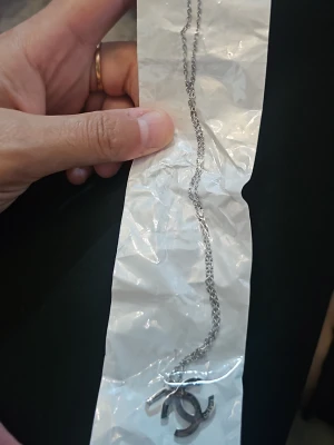 Silverfärgat halsband med CC-hänge - Snyggt halsband i silverfärg med ett klassiskt CC-hänge. Kedjan är tunn och elegant, perfekt för att ge en stilren touch till din outfit. Hänget har en modern design och halsbandet passar till många olika stilar.