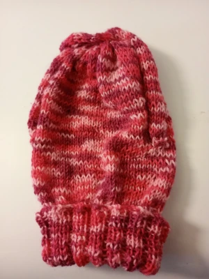Rosa-röd stickad mössa stl S/M - Mysig handstickad mössa i olika nyanser av rosa och rött. Mössan har ett melerat mönster och en bred, ribbstickad kant. Toppen är dekorerad med en knut för extra detalj. Perfekt för kalla dagar och ger en färgklick till din outfit. Tvättråd 40 grader och material Polyester och Akryl,bomull.