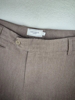 Les Deux byxor beige/gråbruna dress pants chinos storlek 34 - Snygg modell som funkar både till vardags, kontor, fest eller smart casual.   Byxorna har knapp och dragkedja framtill, bälteshällor, sidofickor och passpoalfickor bak.  Broderad Les Deux-detalj bak.  Uppviket längst ner är orginal och "insytt"   Inga fläckar.   Från midja till benslut ca 100cm.   63% polyester, 32% viskos och 5% elastan.  Samfrakta med fler saker från min butik, ta en kik vettja!