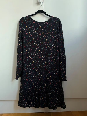 ZARA - Svart långärmad klänning med färgglatt mönster - Svart klänning med lång ärm och färgglatt abstrakt mönster i gult, rött, grönt och rosa. Klänningen har en lös passform och volang längst ner. Perfekt för dig som gillar färg och vill sticka ut lite extra.