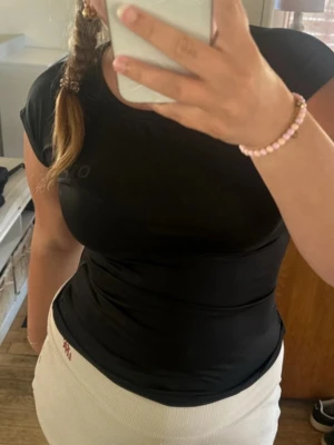 Svart tight t-shirt med kort ärm - Säljer en svart t-shirt med tight passform och korta ärmar. T-shirten har en enkel design med rund halsringning och diskret logga på bröstet. Perfekt till jeans eller kjol för en clean look.
