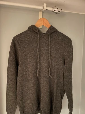 Mörkgrå Kashmir hoodie - Mörkgrå Kashmir hoodie som passar till nästan alla tillfällen. Märket är okänt, då jag har klippt bort lappen och köpt den för cirka 1 år sen. Den ger en avslappnad men samtidigt snygg look och är perfekt att ha på sig i vardan. 