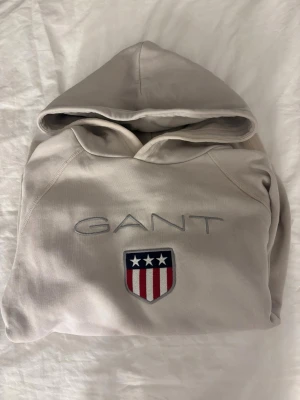 Ljusrosa hoodie från GANT med logga - Snygg ljusrosa hoodie från GANT med broderad logga och amerikanskt inspirerat märke på bröstet. Klassisk huva och magficka framtill. Perfekt för en avslappnad och stilren look.💕