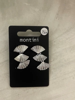 Silvriga solfjäderörhängen Montini - Snygga örhängen från Montini i silverfärgad metall. De har en unik design med tre solfjäderformade delar som hänger i rad och ger ett coolt, modernt intryck. Perfekta för dig som vill sticka ut med accessoarerna och gillar trendiga detaljer.