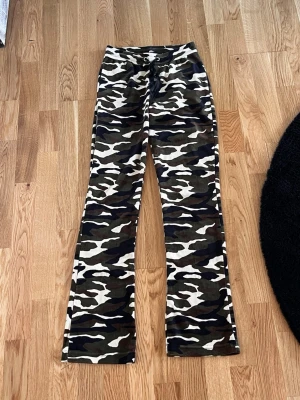 Camo mönstrade mjukisbyxor - Säljer ett par mjukisbyxor med camo-mönster i grönt, beige och svart. Byxorna har dragsko i midjan och raka ben. Perfekta för chill dagar eller när du vill ha en avslappnad stil.