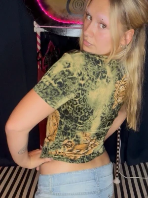 Grön leopardmönstrad t-shirt med lejon - Cool t-shirt i grönt med leopardmönster och stora lejontryck. Modellen är kortärmad och har v-ringning. Materialet känns mjukt och stretchigt, perfekt för en avslappnad och trendig look.