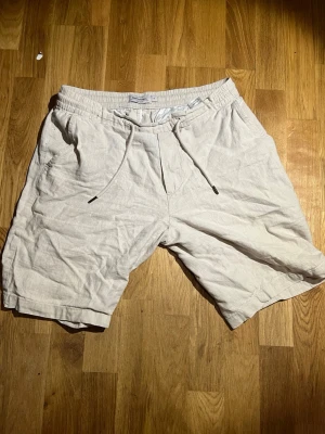 Beiga linneshorts från Dressmann - Snygga beiga shorts från Dressmann i linnemix med avslappnad passform. Shortsen har resårmidja med snörning och två sidofickor. Perfekta för varma dagar och enkel att matcha med t-shirt eller skjorta.