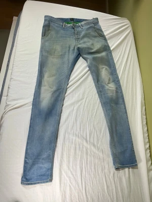 Hugo boss jeans - Säljer ett par ljusblåa slim fit jeans med klassisk femficksdesign och dragkedjegylf. Jeansen har en snygg tvättad look och raka ben. Perfekta för dig som gillar en avslappnad men ändå stilren stil.