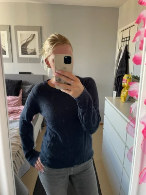 Mörkblå stickad tröja från Vila - Mysig mörkblå stickad tröja från Vila med rund halsringning och långa ärmar. Tröjan har ribbade muddar vid ärmslut och nederkant, vilket ger en klassisk och enkel look. Perfekt att matcha med jeans eller kjol för en avslappnad stil.
