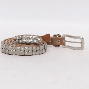 Brunt bälte med silvernitar - Snyggt brunt bälte i skinn med massor av runda silverfärgade nitar längs hela bandet. Bältet har ett klassiskt spänne i silverfärgad metall och passar perfekt för att ge din outfit en cool touch.
