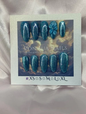 Velora (XS);Meidum Almond - Snygga handgjorda press-on naglar i en djupblå, glittrig färg med en medium lång almondform. Ett av nageltipsen har en handgjord 3D-blomma som detalj vilket ger en unik touch. Perfekt för dig som vill ha något extra till naglarna. Kommer i XS: 14 mm, 11 mm, 11,5 mm, 10 mm, 8 mm