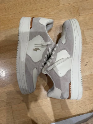 Vita och grå Polo Ralph Lauren sneakers - Användt de 1 gång och de va på ett bröllop annars aldrig använt, de har legat i skåpet sedan dess, skorna kankse ser smutsiga ut på bilden men jag kommer att tvätta de när någon köper.          Snygga sneakers från Polo Ralph Lauren i vitt och ljusgrått. Skorna har mockadetaljer, klassisk låg siluett och Polo-logga på sidan. Yttermaterialet är en mix av läder och mocka, med vita snören och diskreta bruna detaljer vid sulan.