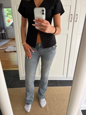 Ljusblå bootcut jeans med låg midja - Säljer ett par ljusblå jeans med bootcut-modell och låg midja. Jeansen har klassiska fem fickor, dragkedja och knapp framtill samt snygga slitningar för en avslappnad look. Perfekta till sneakers eller boots.