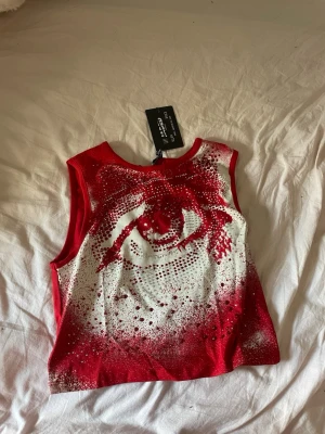 Röd och vit ärmlös topp från Jaded London - Säljer en statement topp från Jaded London i rött och vitt med ett coolt abstrakt mönster och glittriga detaljer. Toppen är ärmlös och croppad, perfekt för att sticka ut. Materialet känns mjukt och stretchigt.