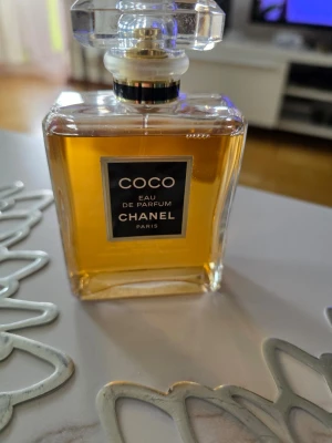 Coco Eau de Parfum från Chanel - Elegant parfymflaska i glas med guld- och svartdetaljer, innehållande den klassiska doften Coco Eau de Parfum från Chanel. Flaskan har en fyrkantig form och genomskinligt lock som ger en lyxig känsla. Perfekt för dig som gillar exklusiva dofter.