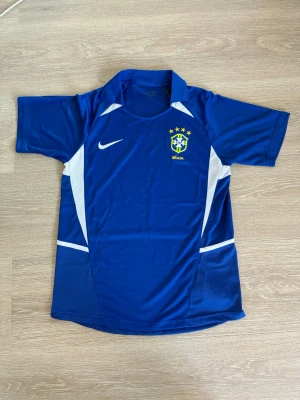 Blå Brasilien Nike fotbollströja - Snygg blå fotbollströja från Nike med Brasilien-emblem på bröstet och vita detaljer längs sidorna. Tröjan har korta ärmar, krage och är tillverkad i ett lätt, ventilerande material som passar perfekt till träning eller match.